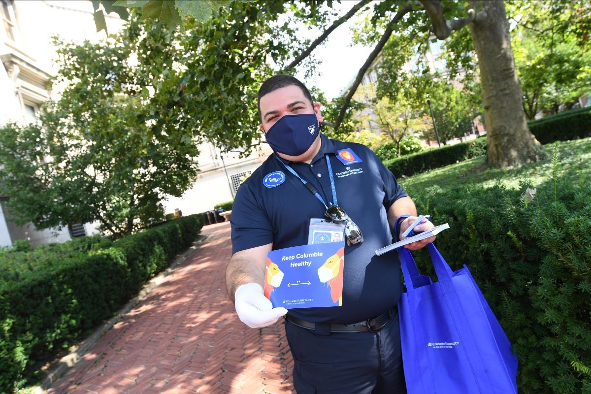 Columbia staff member volunteering as a Stay Healthy Ambassador wearing a face covering while passing out postcards to new arrivals on campus for the fall semester