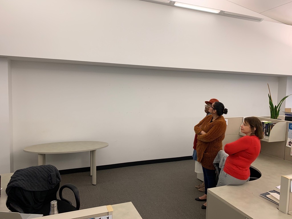 "Before" photo of the ISERP space. A group of people stand off to the side and look at a large, blank, white wall in their newly-renovated but empty office.