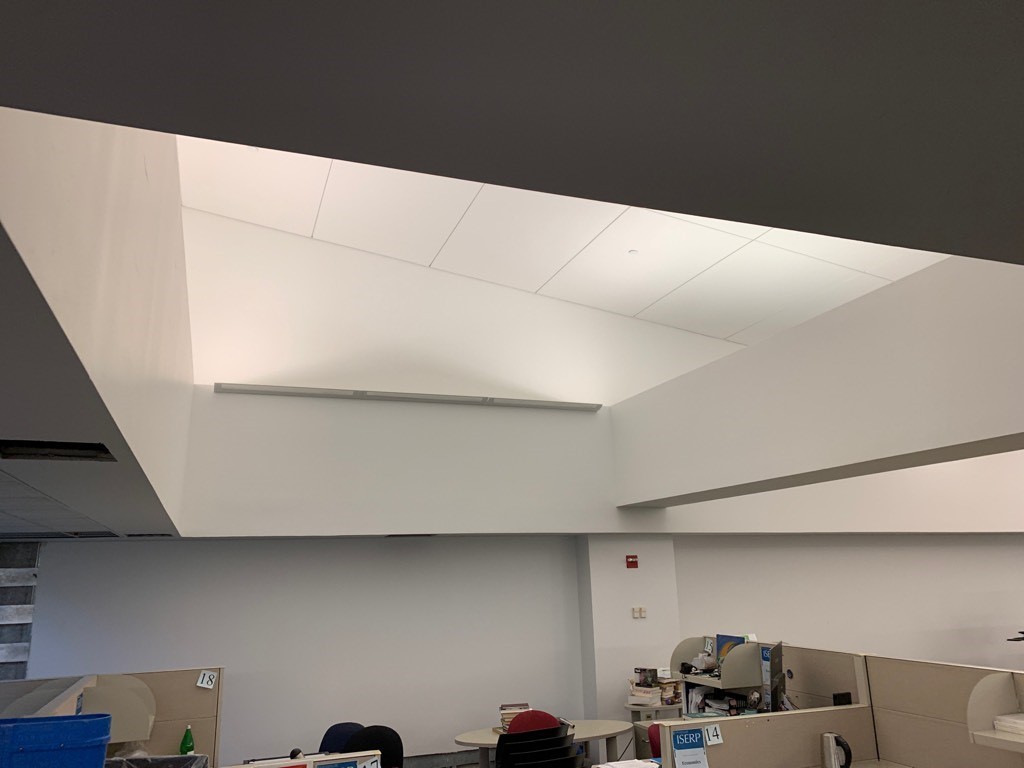 "Before" photo of the ISERP space. A slanted ceiling with surrounded white walls in an office space with some empty cubicles down below. The space was recently renovated and appears overly blank and white.